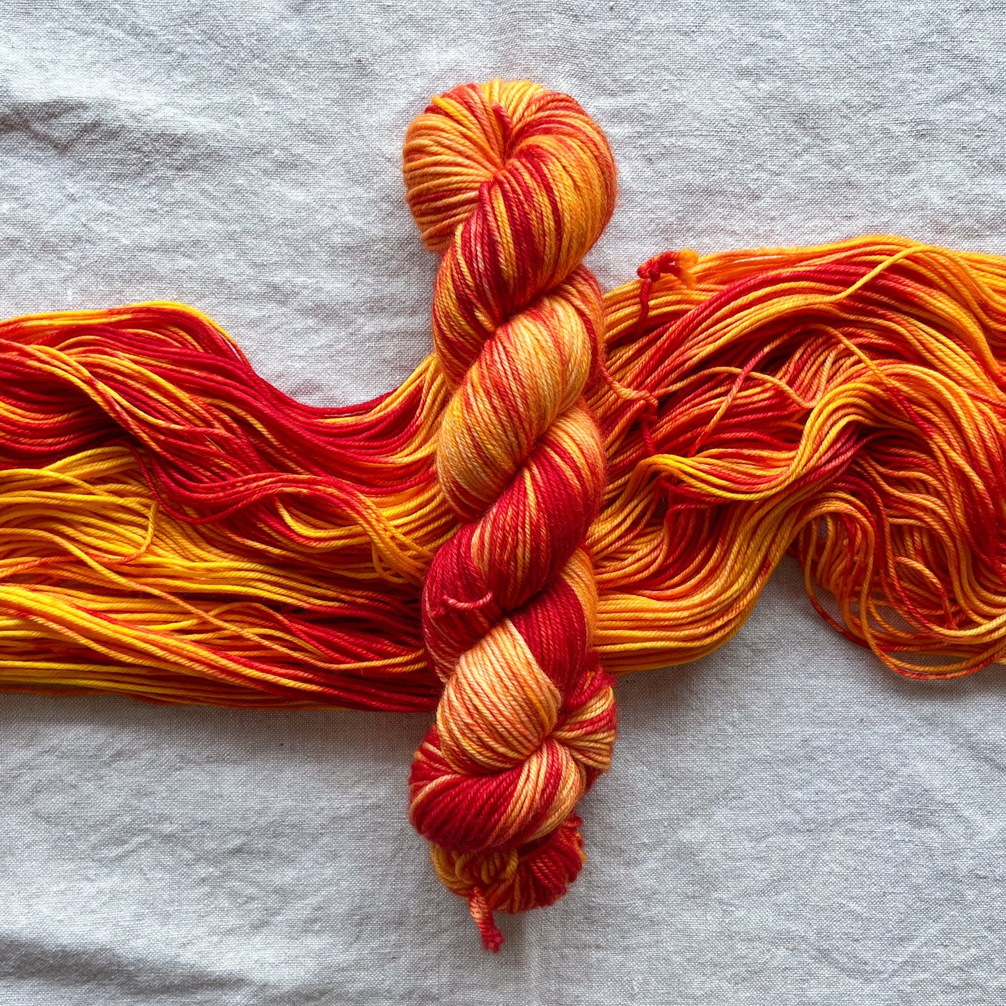 A fiery hand dyed yarn with a glowing yellow base shot through with fiery red. The yarn is in a twisted skein on top of an open untwisted skein.