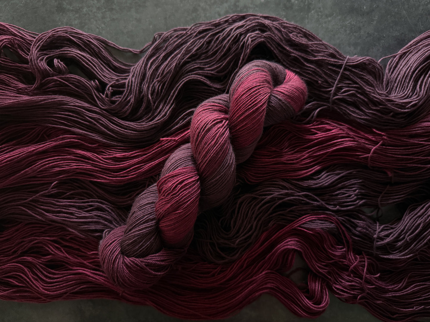 Skein of dark red yarn on top of open skeins of the same yarn on a textured gray background