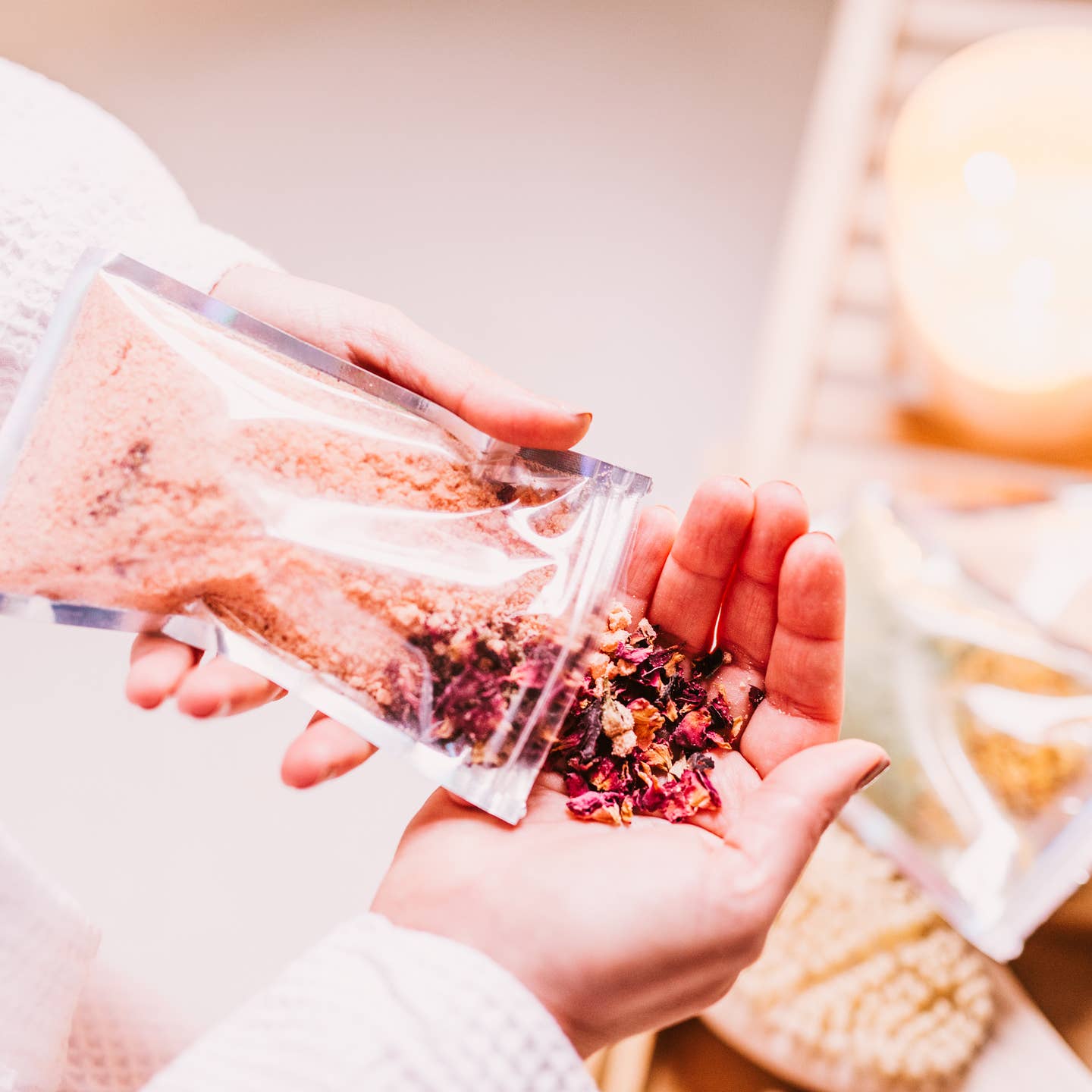 Person holding a small container of pink and red dried flowers over their palm.