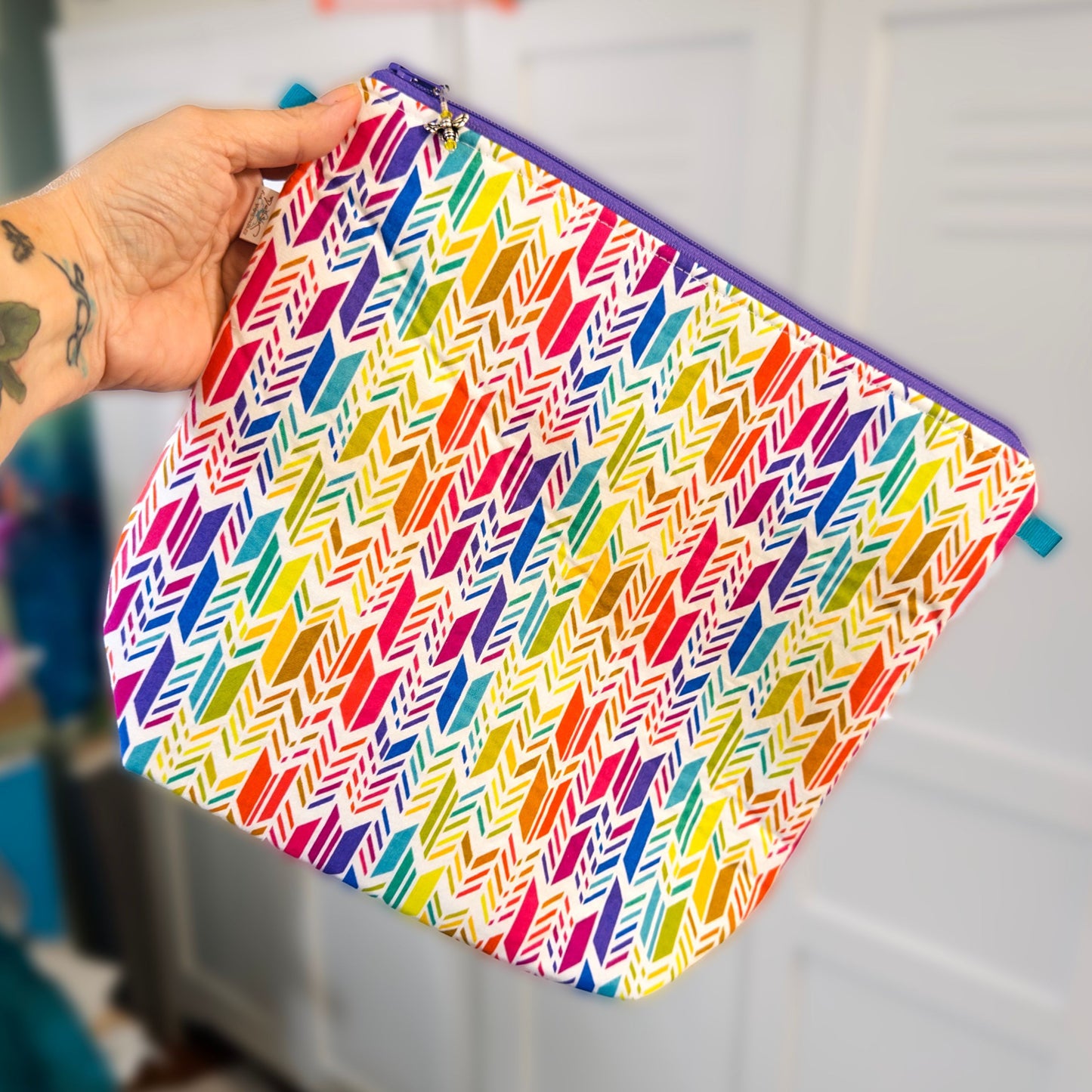 Knitting project bag with a rainbow abstract feather pattern held by a hand against a neutral background