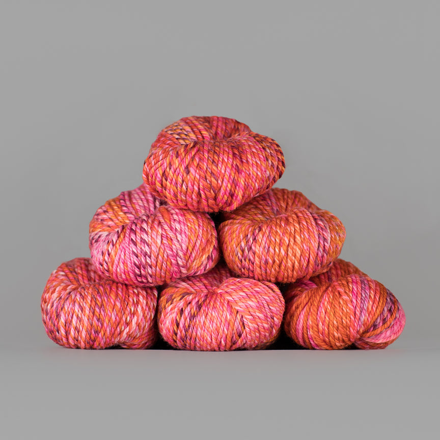 Stack of multicolored pink, orange and peach yarn skeins on a gray background