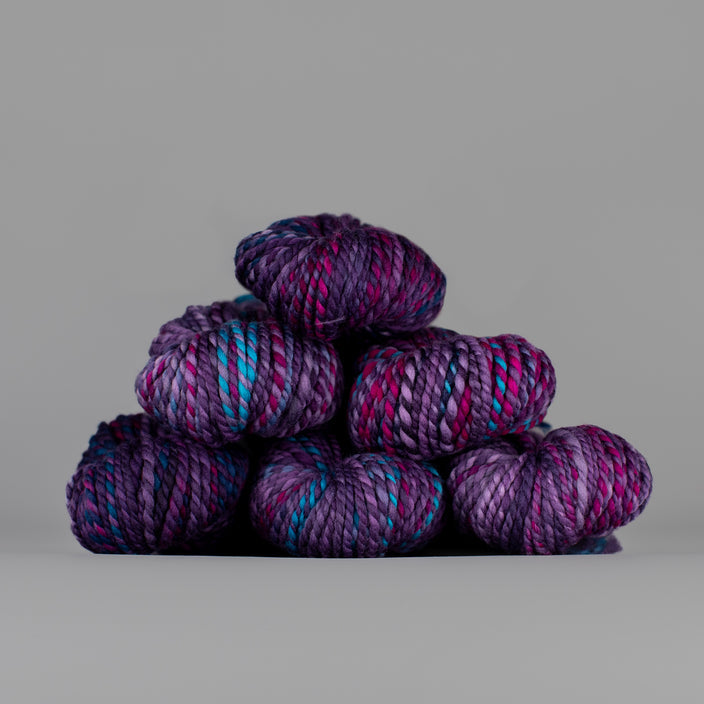 Skeins of Spincycle Plump Bulky weight yarn in dark purple, mauve, and blue color gradient