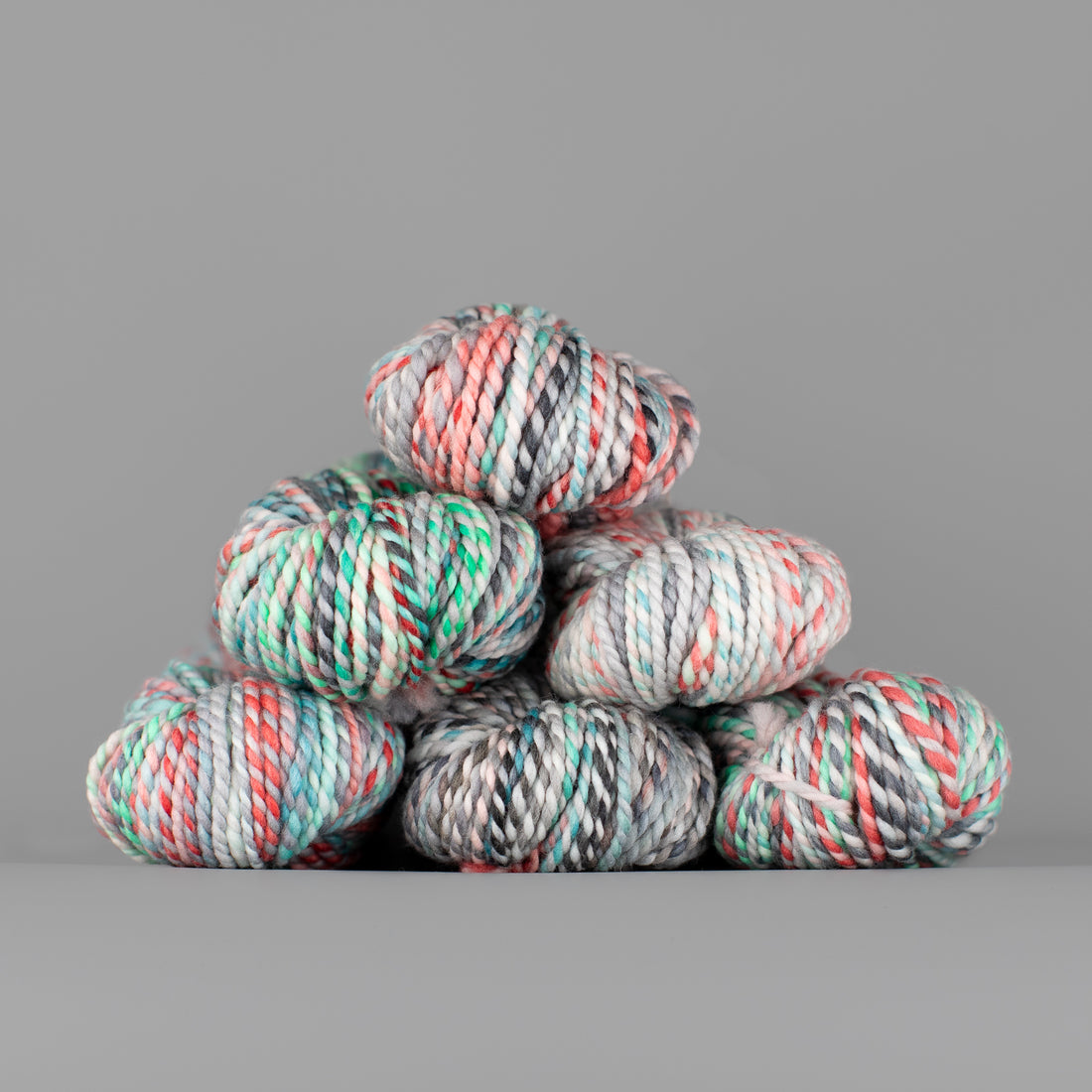 Skeins of Spincycle Plump Bulky weight yarn in white, pink, grey, green, and blue color gradient