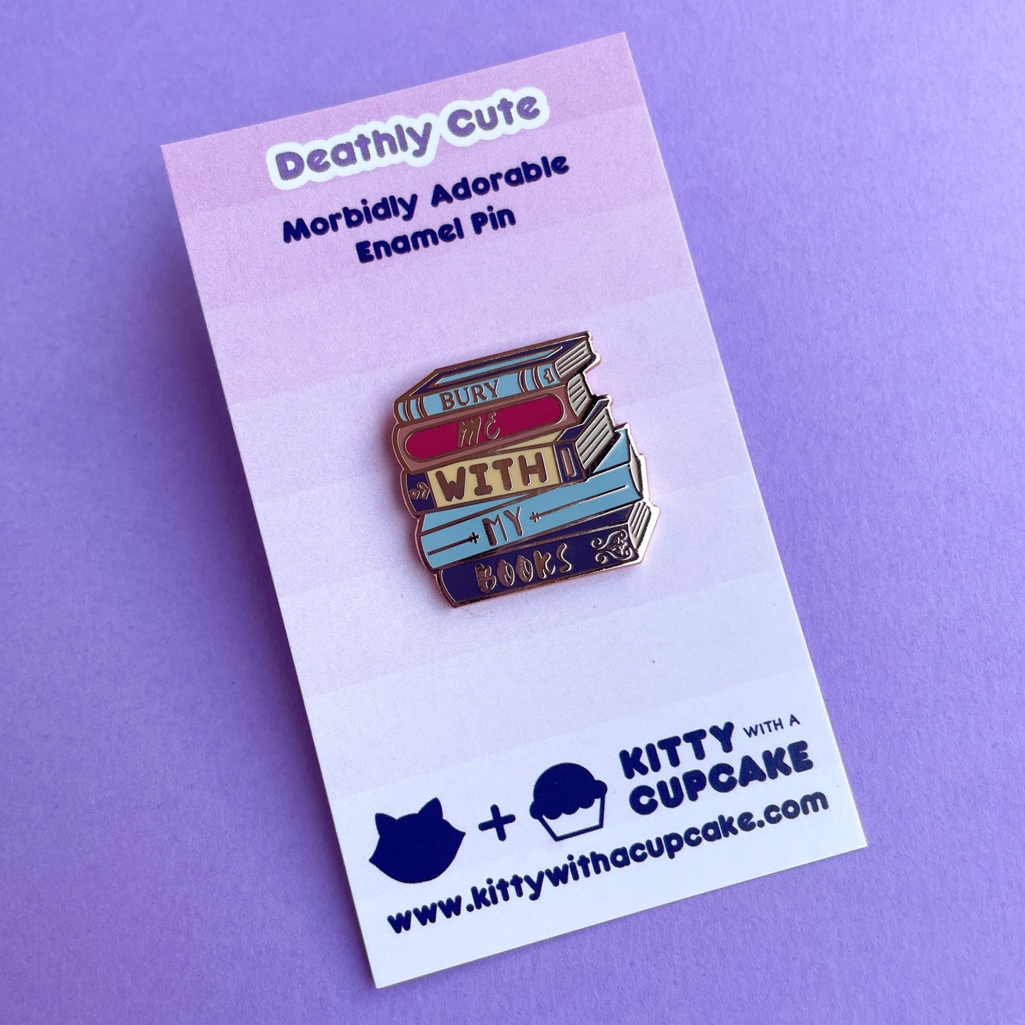An enamel pin shaped like a stack of books that reads "Bury Me With My Books" on a pink card.