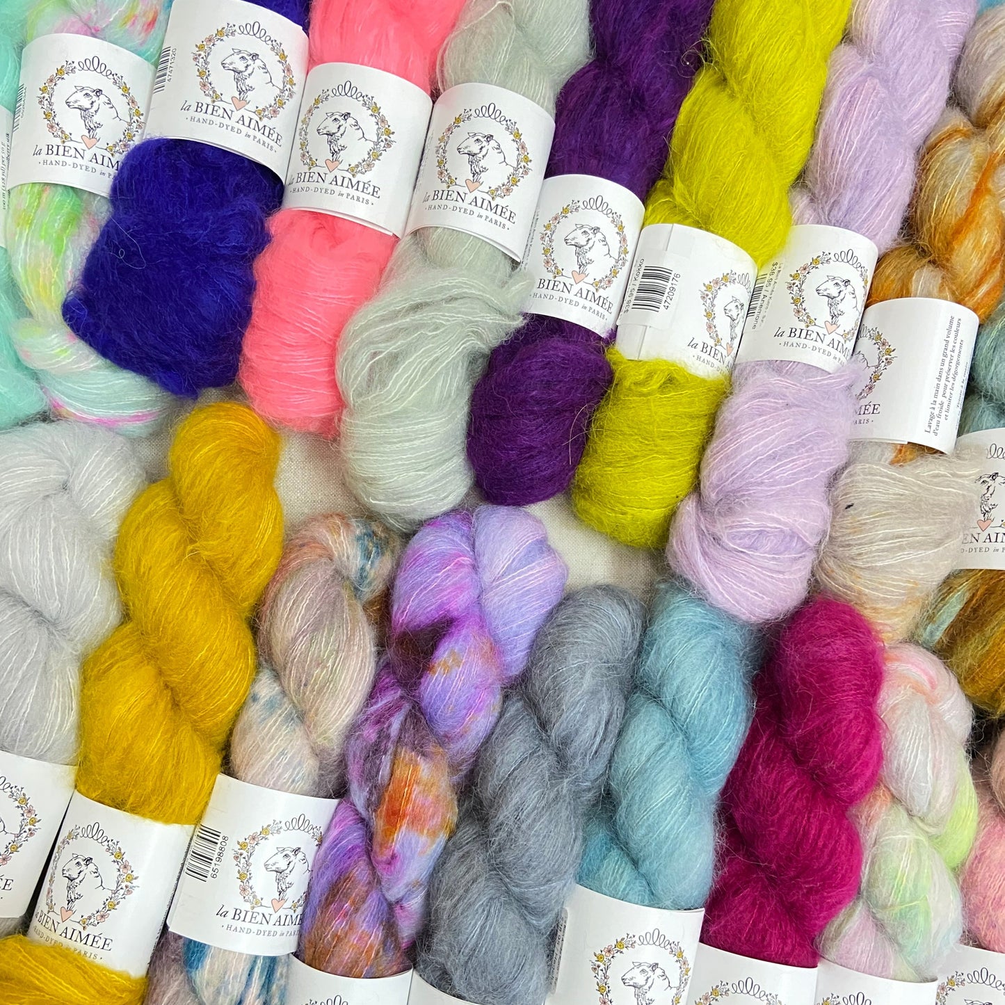 An image of multiple skeins of La Bien Aimee lace weight yarn in a variety of colors with white ‘La Bien Aimee’ labels.