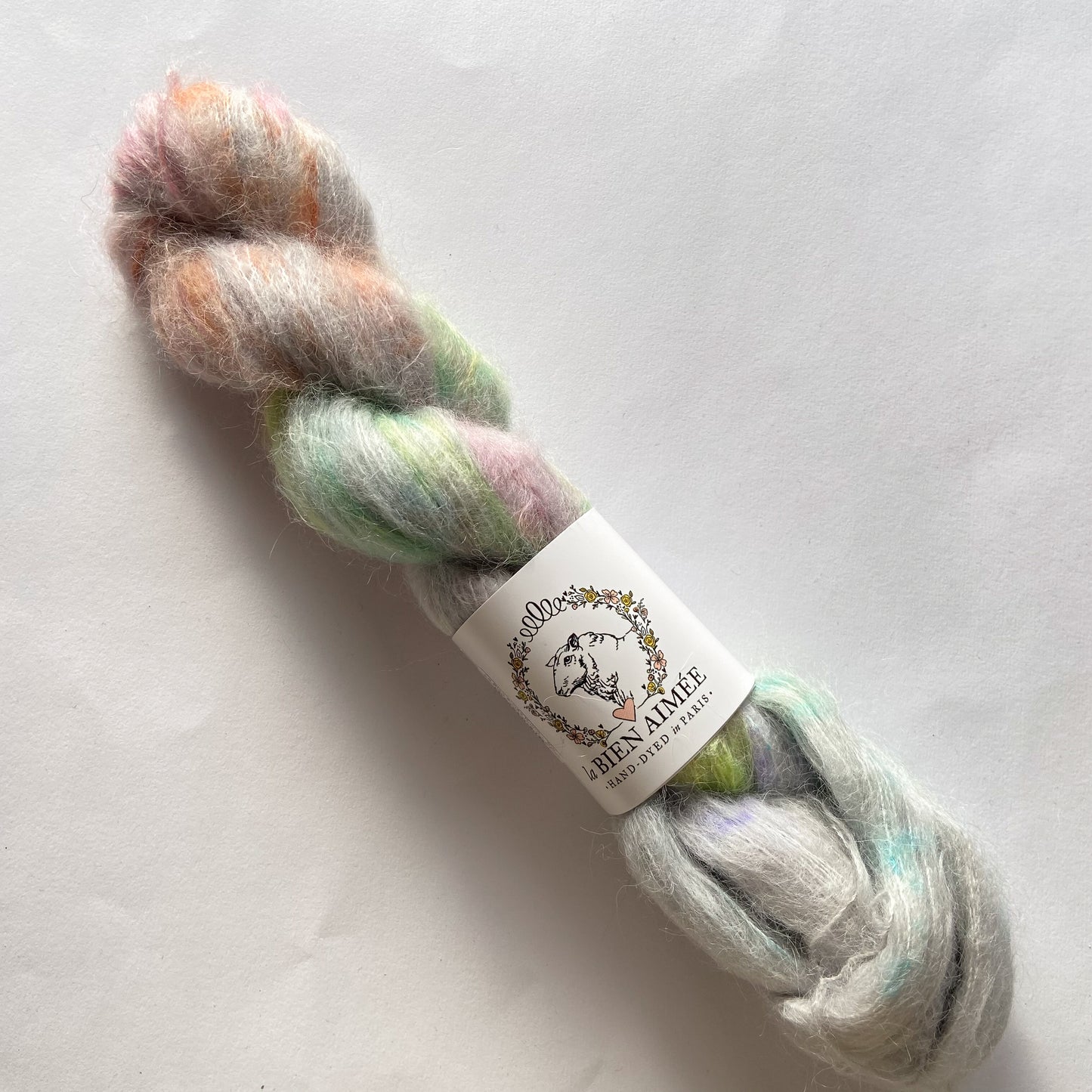 An image of a skein of La Bien Aimee lace weight yarn in a pale gray base with green, orange, and pink colors, and a white ‘La Bien Aimee’ label against a white background.