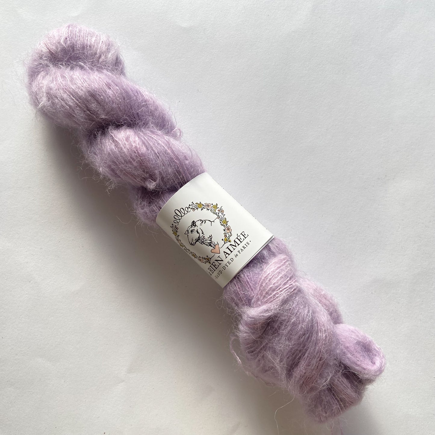 An image of a skein of La Bien Aimee lace weight yarn in a pale purple color with a white ‘La Bien Aimee’ label against a white background.