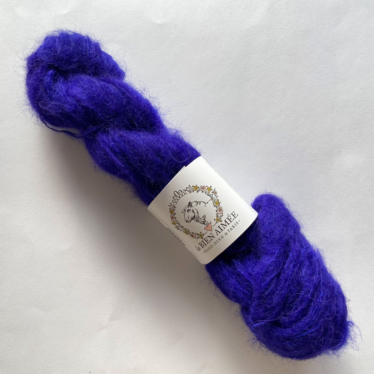 An image of a skein of La Bien Aimee lace weight yarn in a vibrant blue color with a white ‘La Bien Aimee’ label against a white background.