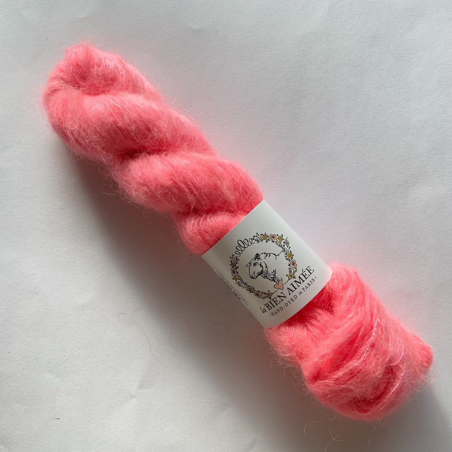 An image of a skein of La Bien Aimee lace weight yarn in a neon pink color with a white ‘La Bien Aimee’ label against a white background.