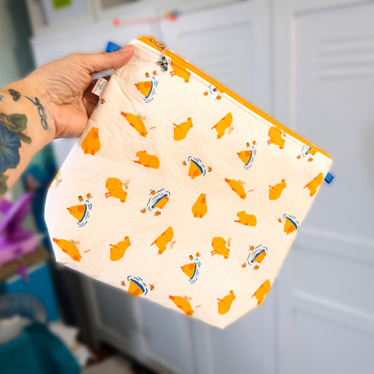 A zippered knitting project bag with a cute cabypara print, held by a hand against a neutral backgroudn