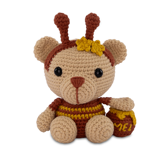 Crocheted bear plush toy with honey jar and bee costume on a white background