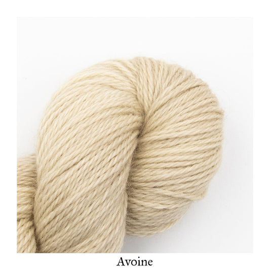 A close-up image of a skein of La Bien Aimee worsted weight yarn in a cream color labeled ‘Avoine’ against a white background.