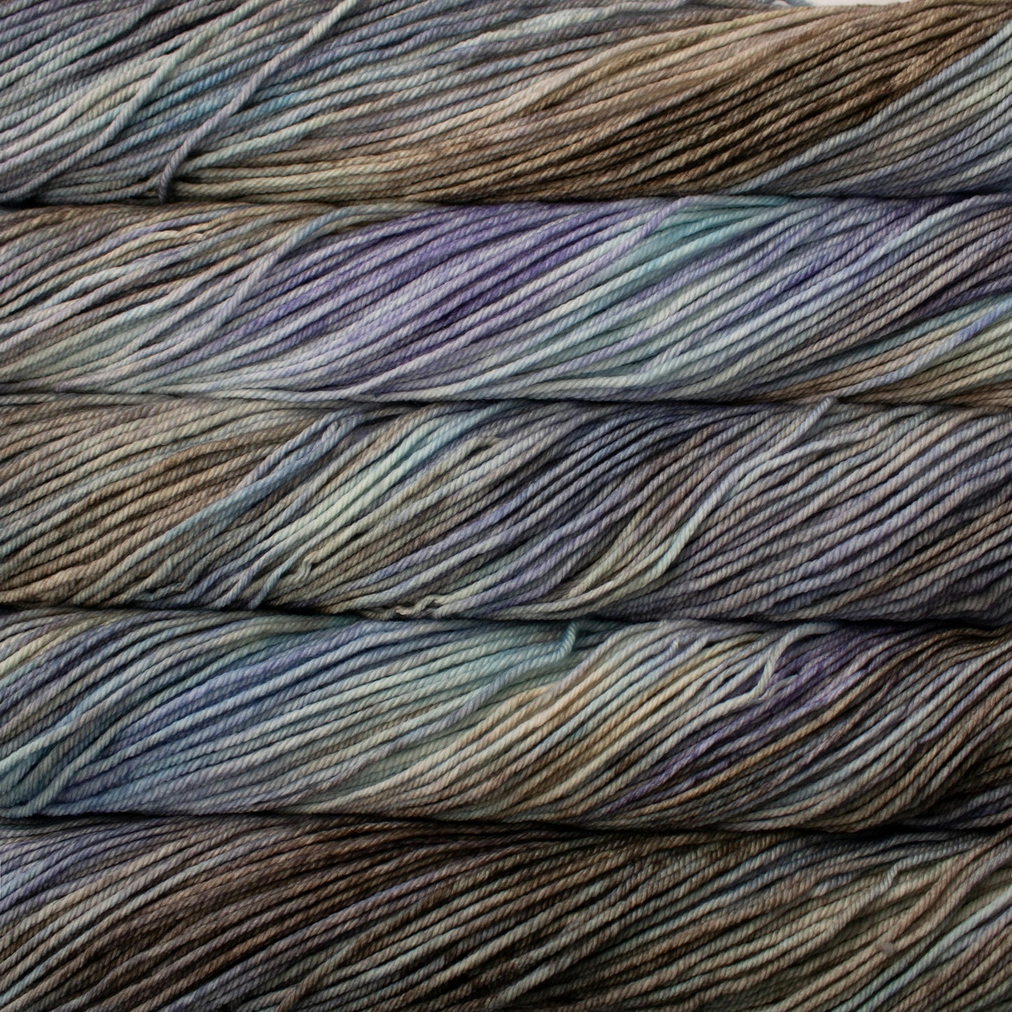 A close up of skeins of Malabrigo Rios worsted weight yarn in grey, blue, and beige colors