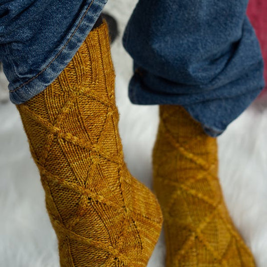 Yellow knitted socks with a diamond pattern worn by a person on a white background