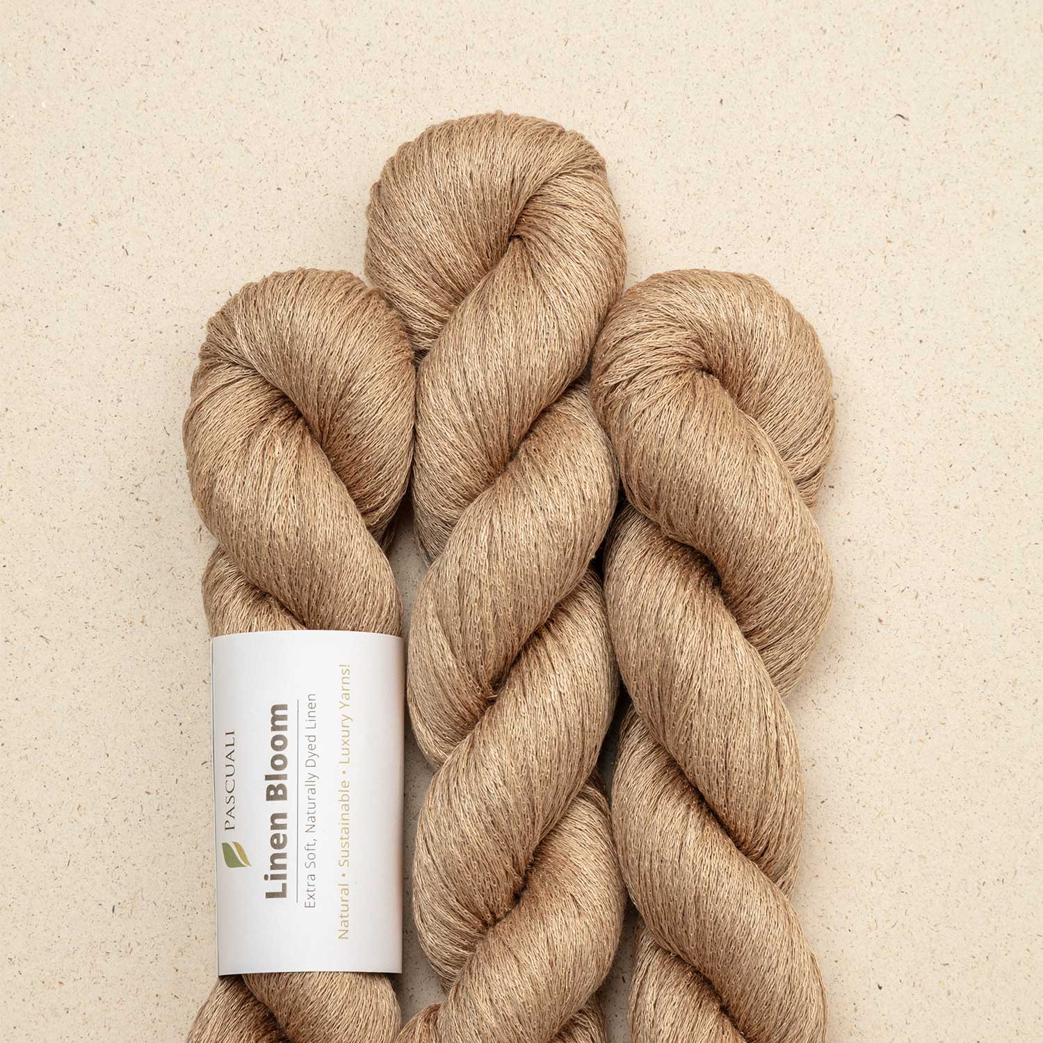 Hanks of light brown yarn with 'Linen Bloom' tag on a beige background