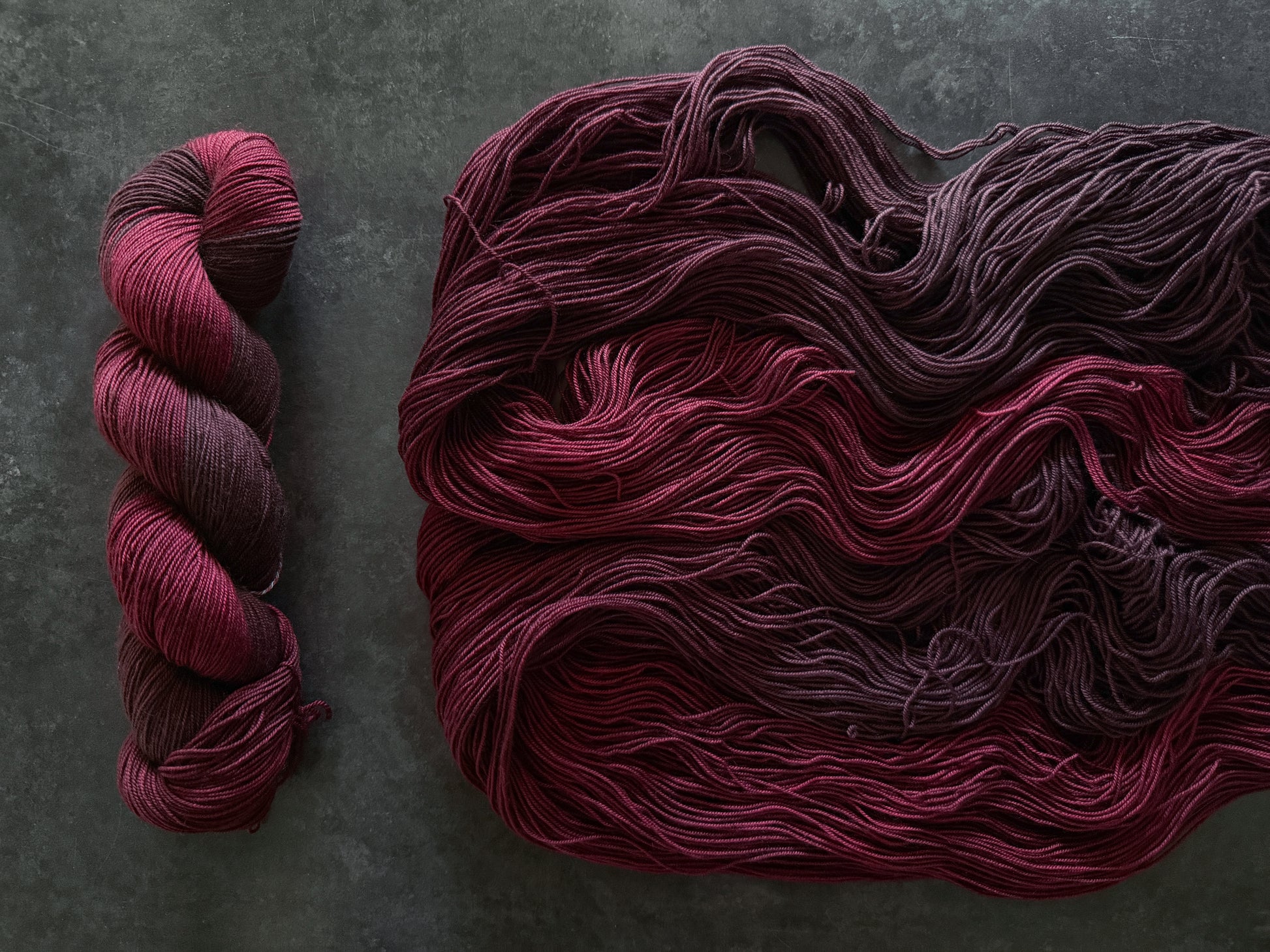 Skeins of dark red yarn on a textured gray background