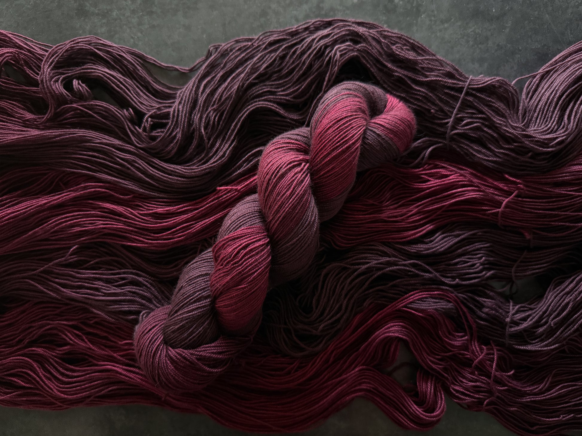 Skein of dark red yarn on top of open skeins of the same yarn on a textured gray background