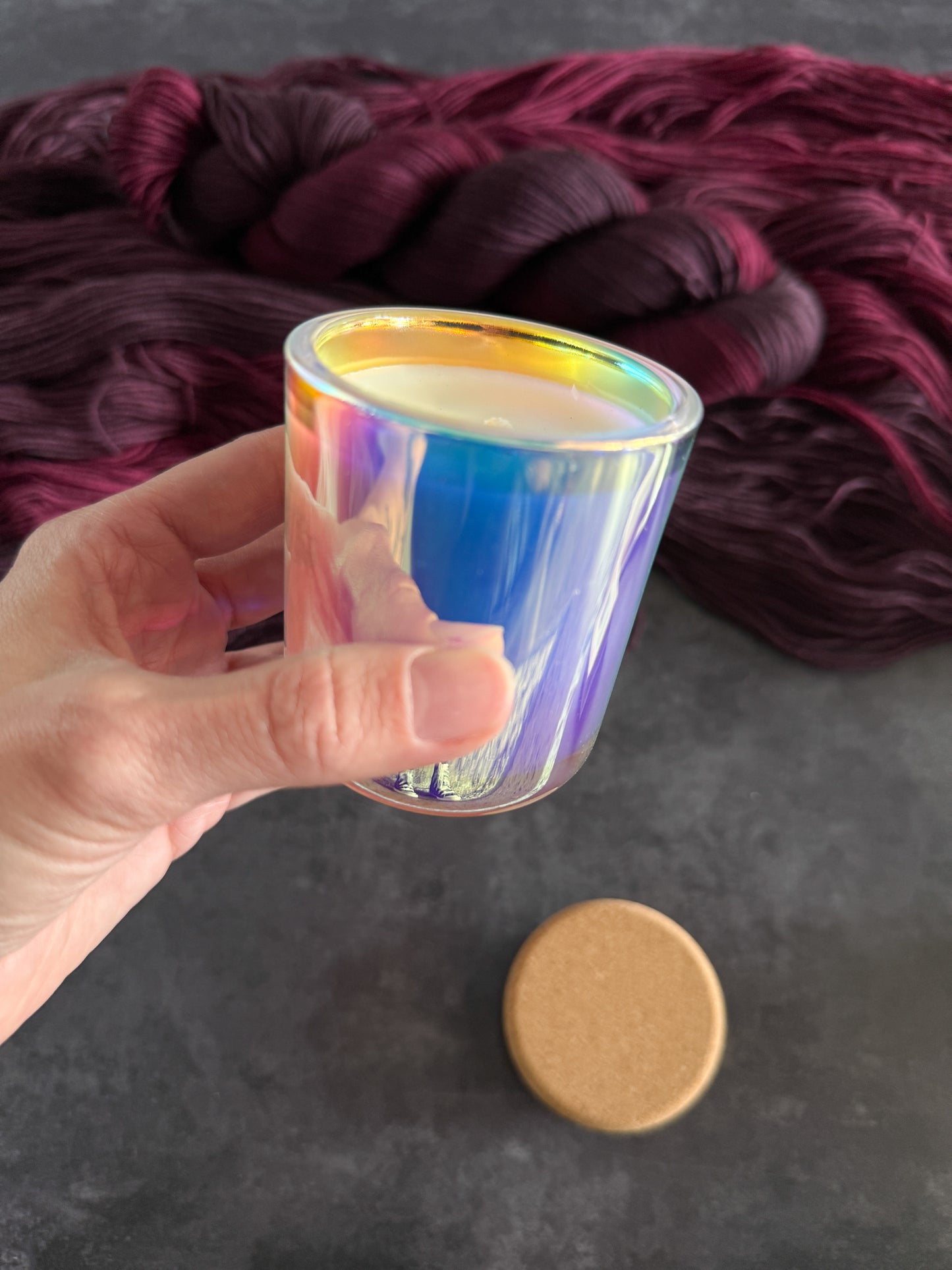 Hand holding a iridescent glass jar candle with a dark red yarn in the background