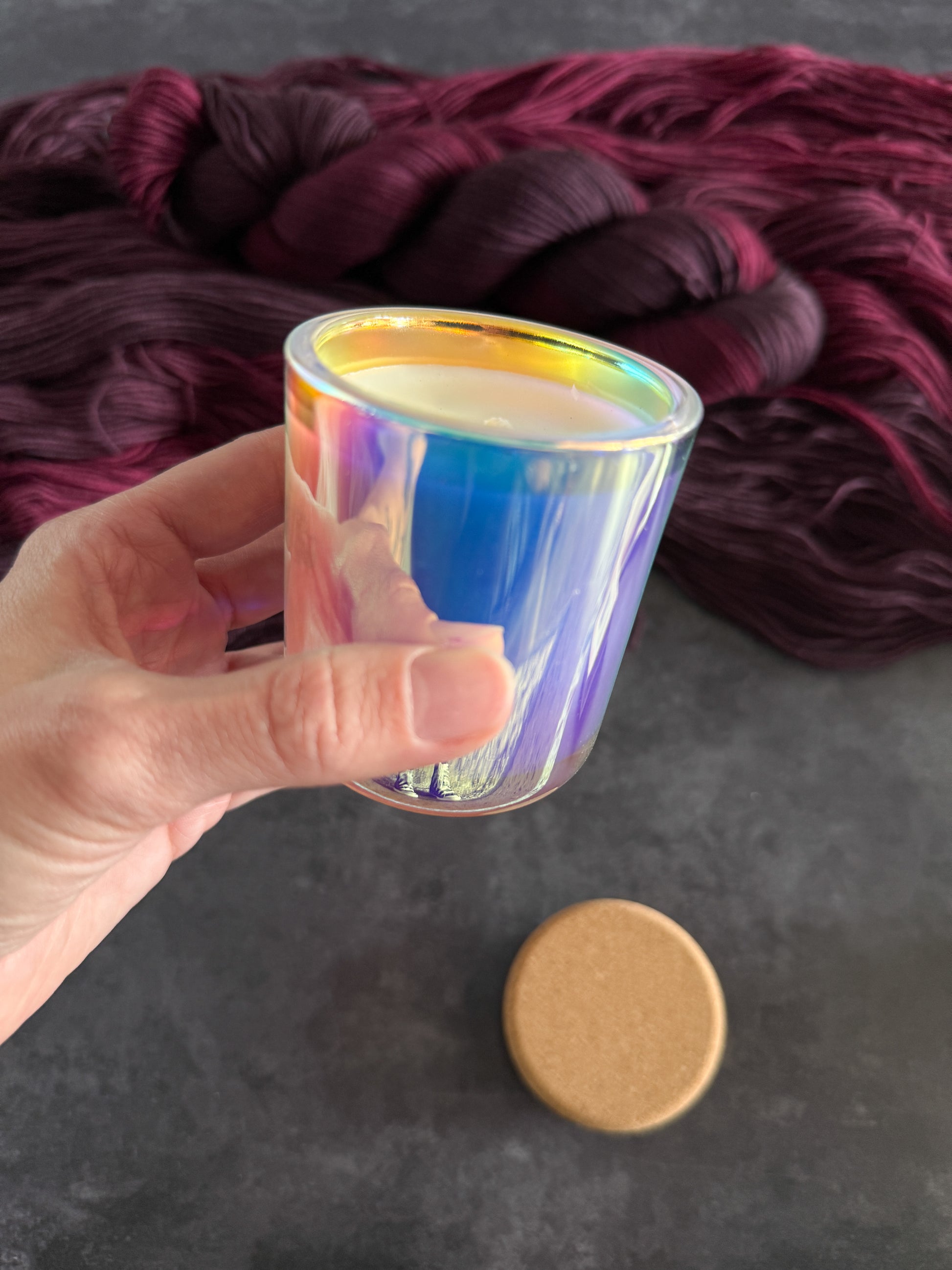 Hand holding a iridescent glass jar candle with a dark red yarn in the background