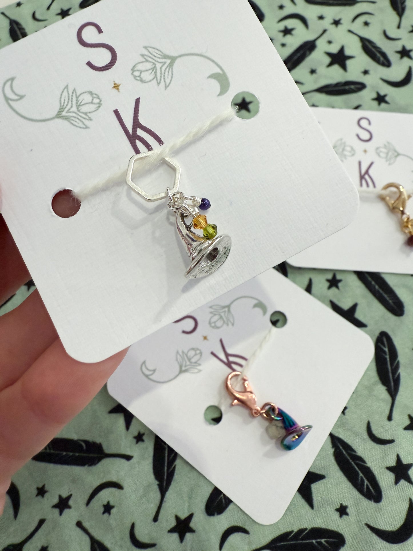 Jewelry cards with small witch hat charms on a patterned background