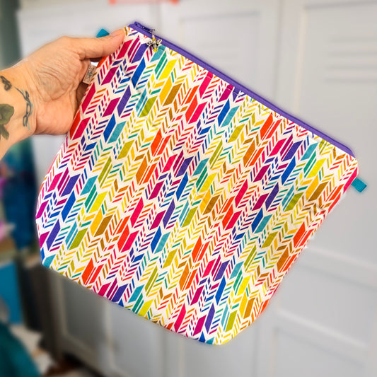 Knitting project bag with a rainbow abstract feather pattern held by a hand against a neutral background