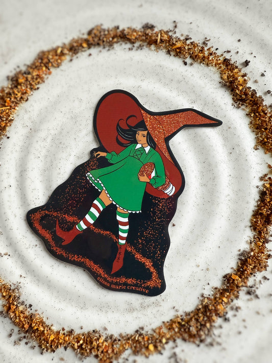 Glittery sticker showing a girl in a green dress and red witch hat, spilling a circle of Tajin around her