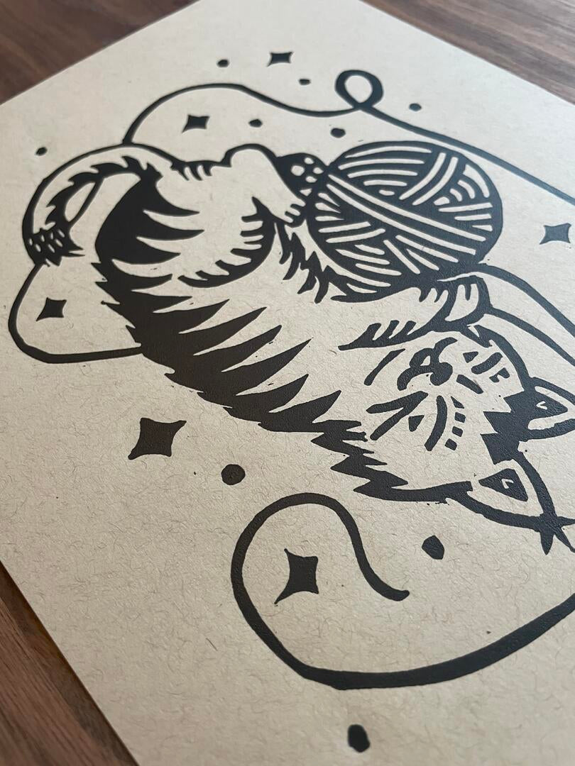 Black ink drawing of a cat with yarn on beige paper