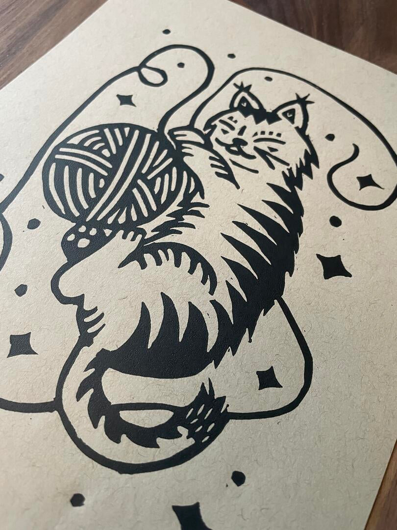 Black ink illustration of a cat playing with yarn on beige paper.