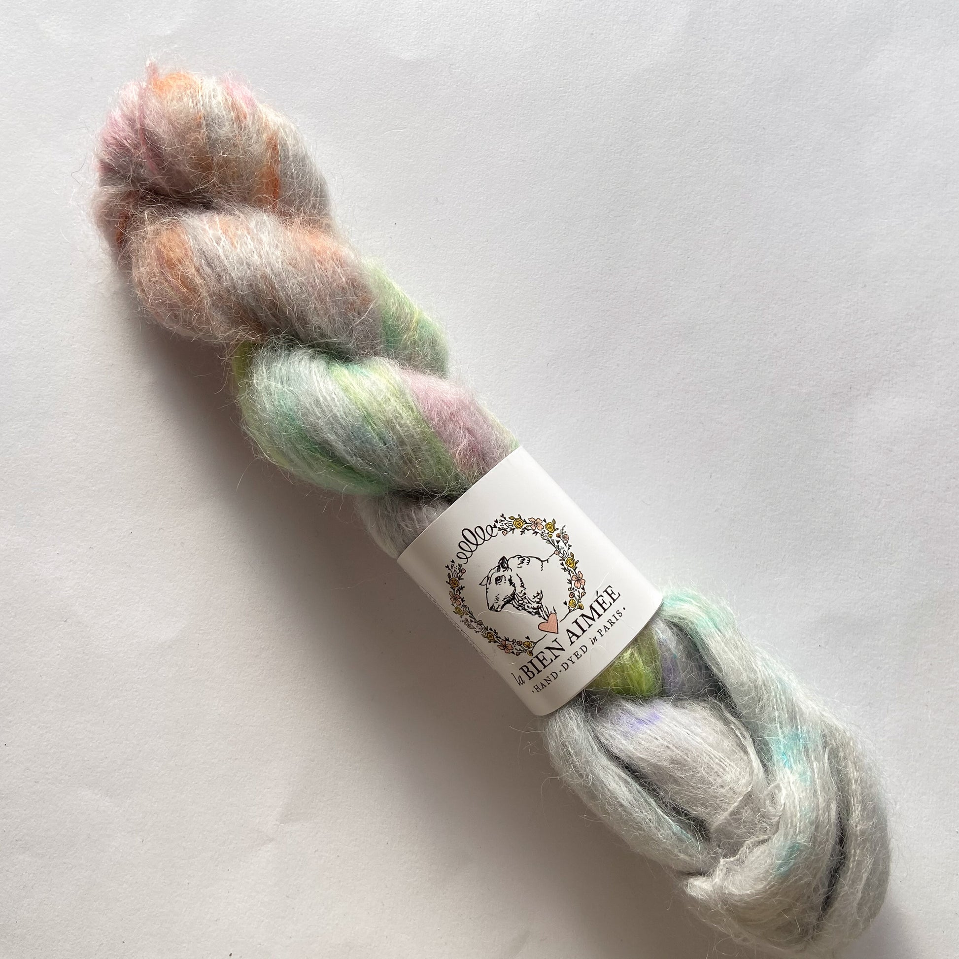 An image of a skein of La Bien Aimee lace weight yarn in a pale gray base with green, orange, and pink colors, and a white ‘La Bien Aimee’ label against a white background.