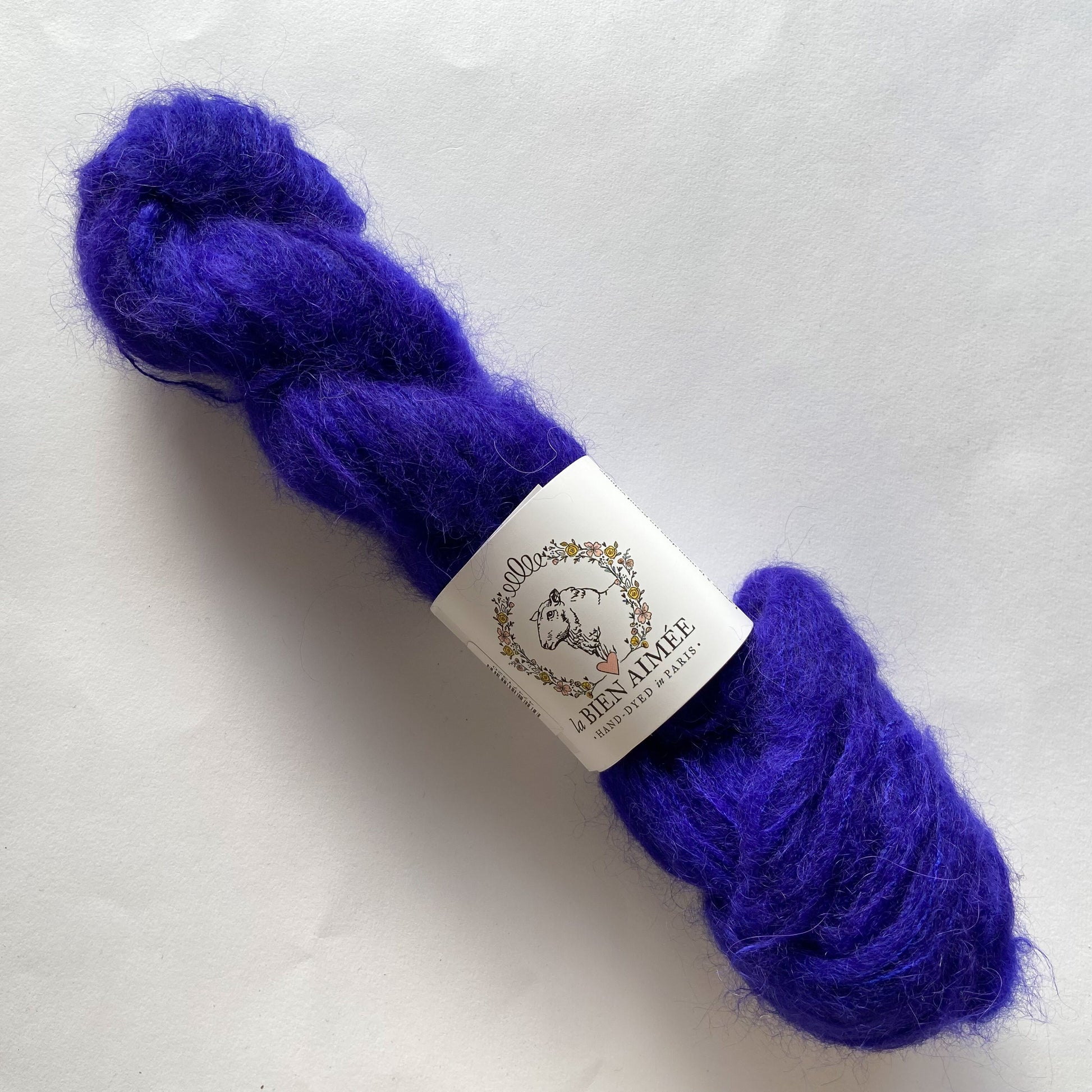 An image of a skein of La Bien Aimee lace weight yarn in a vibrant blue color with a white ‘La Bien Aimee’ label against a white background.