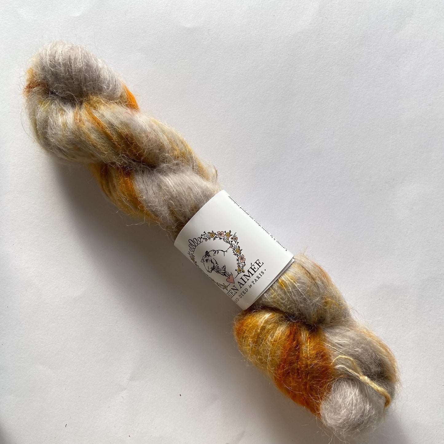 An image of a skein of La Bien Aimee lace weight yarn in the colors beige, yellow, and orange with a white ‘La Bien Aimee’ label against a white background.