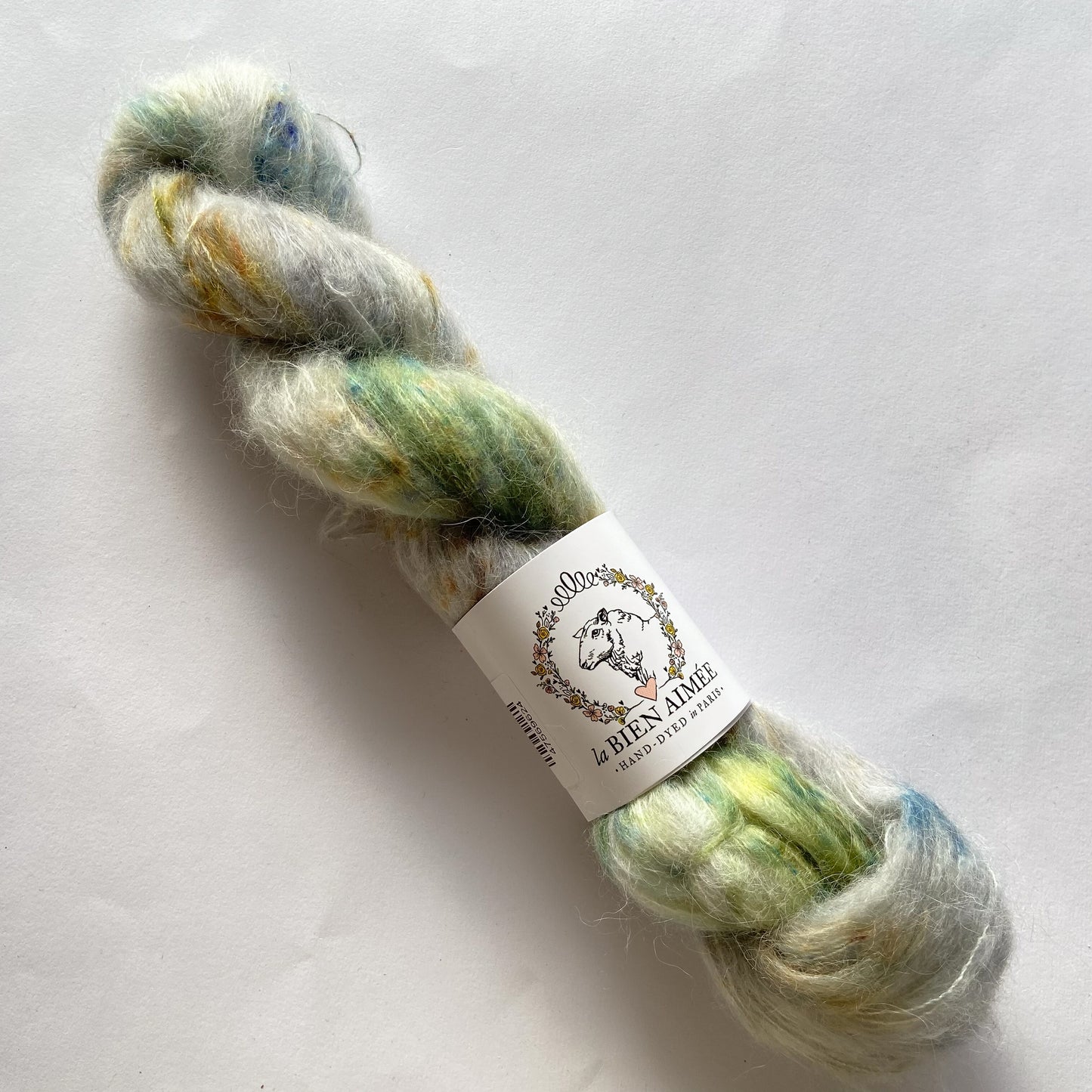 An image of a skein of La Bien Aimee lace weight yarn in the colors gray, green, blue, and yellow with a white ‘La Bien Aimee’ label against a white background.