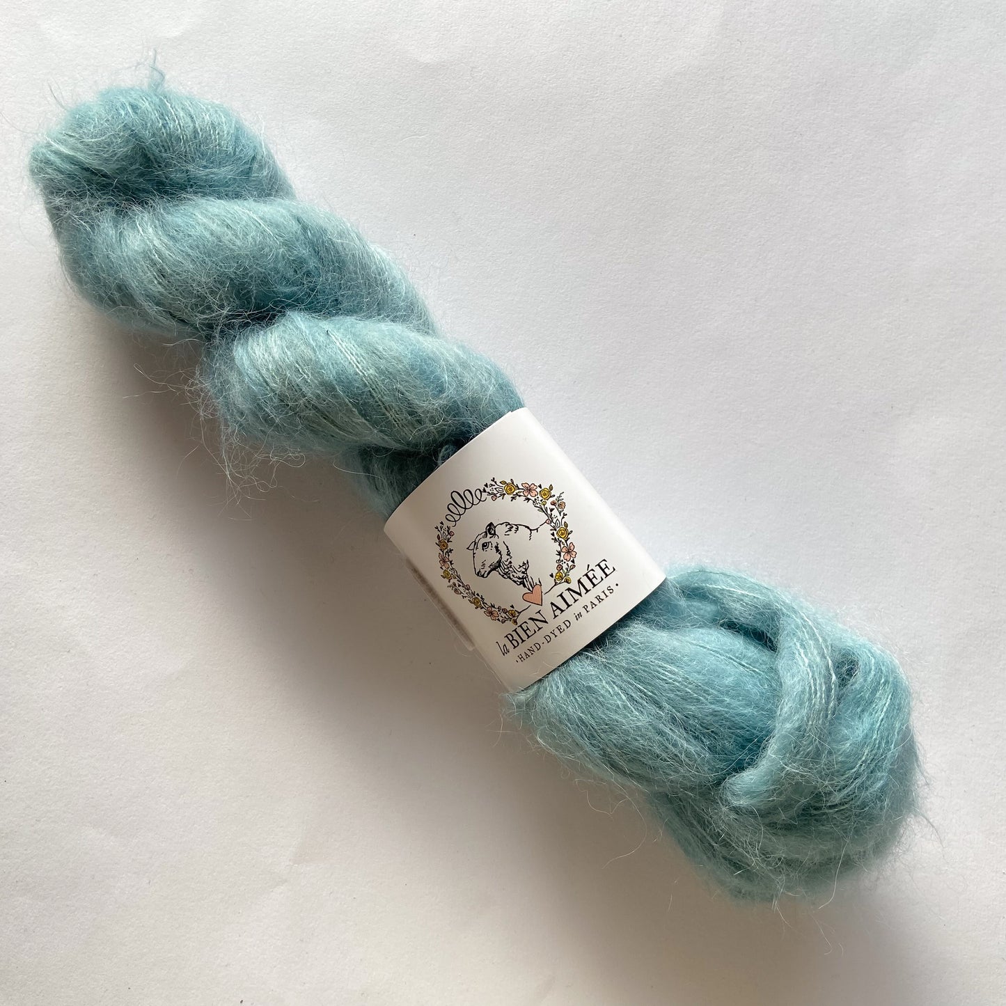 An image of a skein of La Bien Aimee lace weight yarn in a sky blue color with a white ‘La Bien Aimee’ label against a white background.