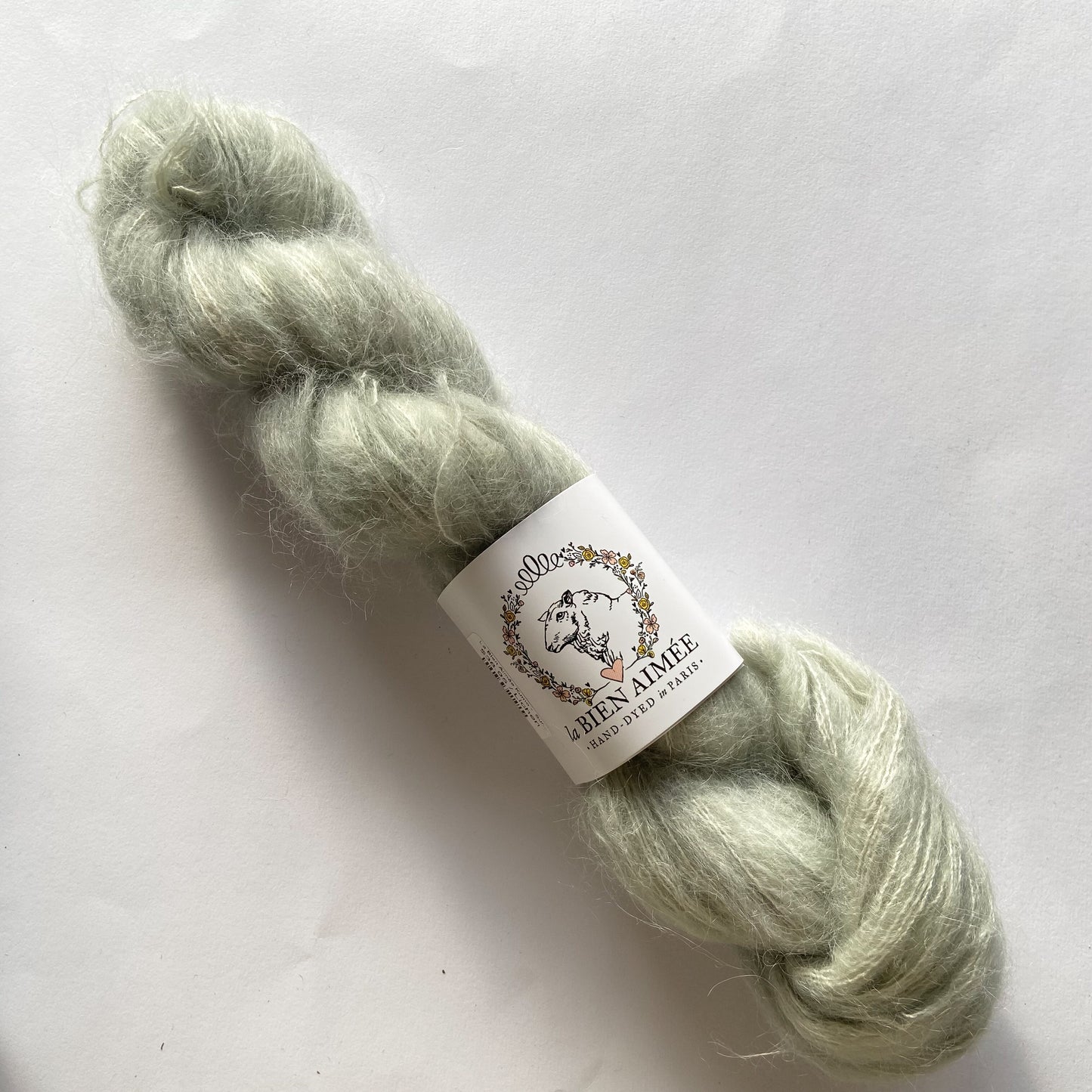 An image of a skein of La Bien Aimee lace weight yarn in a pale gray color with a white ‘La Bien Aimee’ label against a white background.