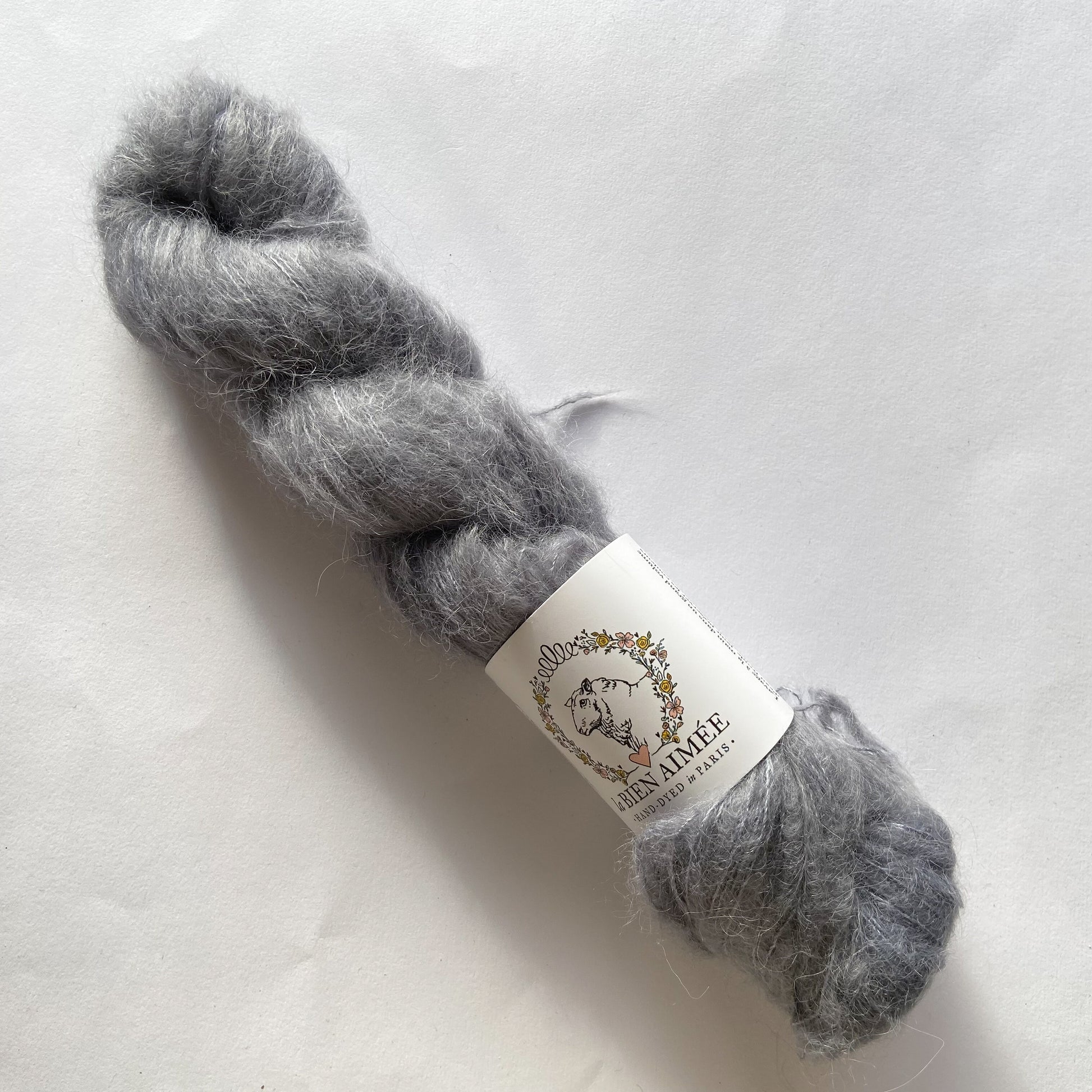 An image of a skein of lace weight yarn in a gray color with a white ‘La Bien Aimee’ label against a white background.
