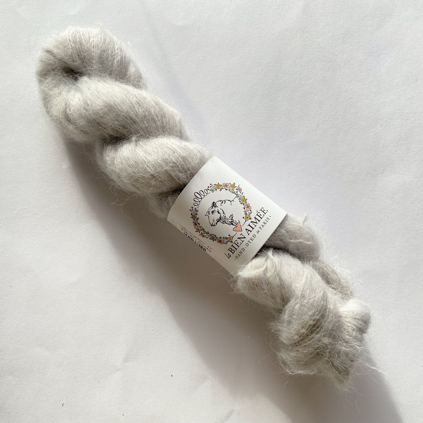 An image of a skein of lace weight yarn in an off-white color with a white ‘La Bien Aimee’ label against a white background.