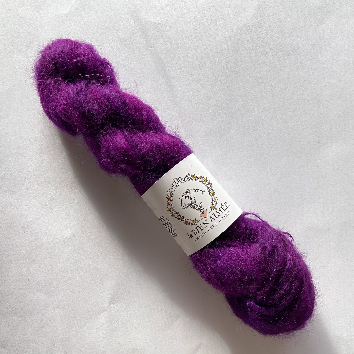An image of a skein of lace weight yarn in a deep purple color with a white ‘La Bien Aimee’ label against a white background.