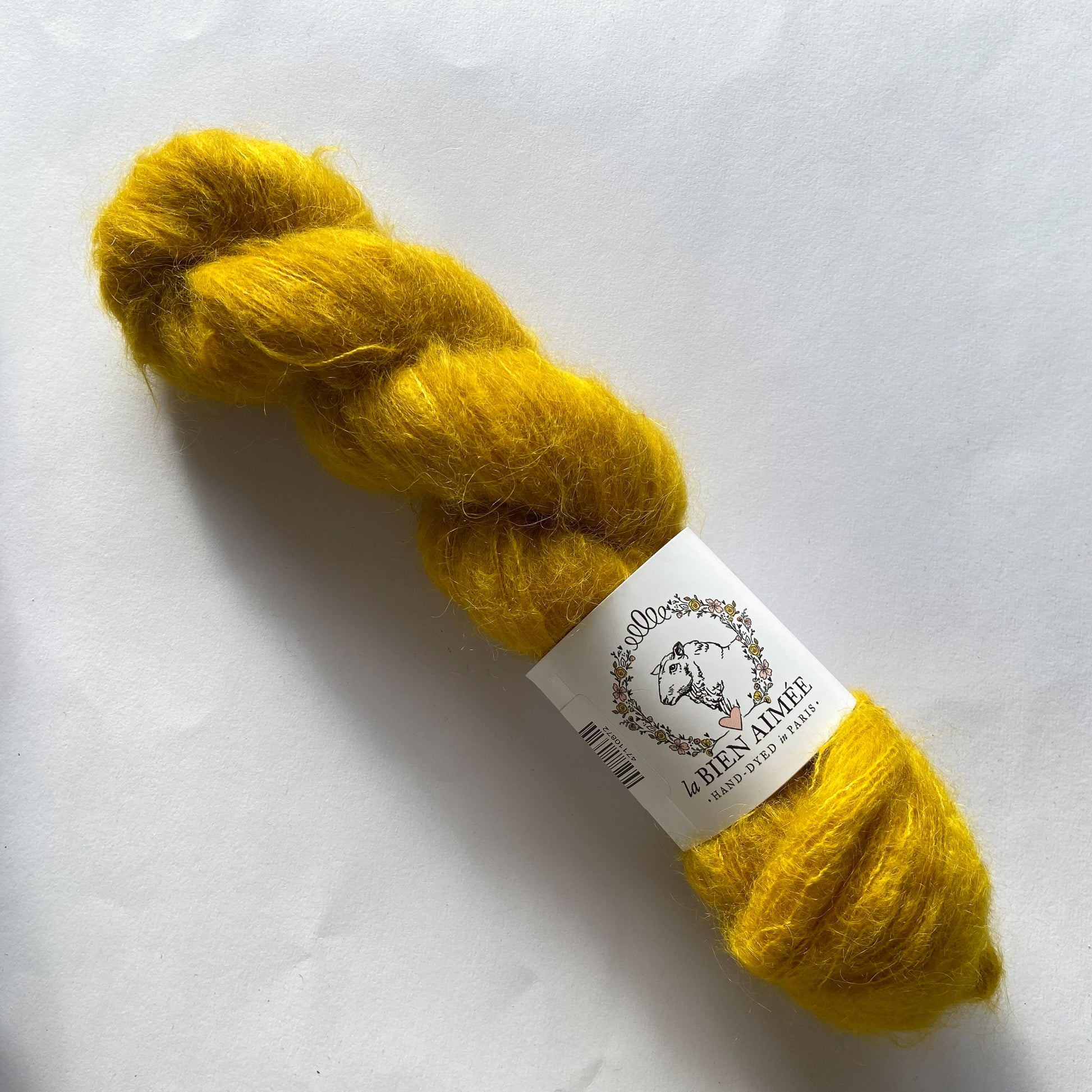 An image of a skein of lace weight yarn in a vibrant mustard yellow color with a white ‘La Bien Aimee’ label against a white background.