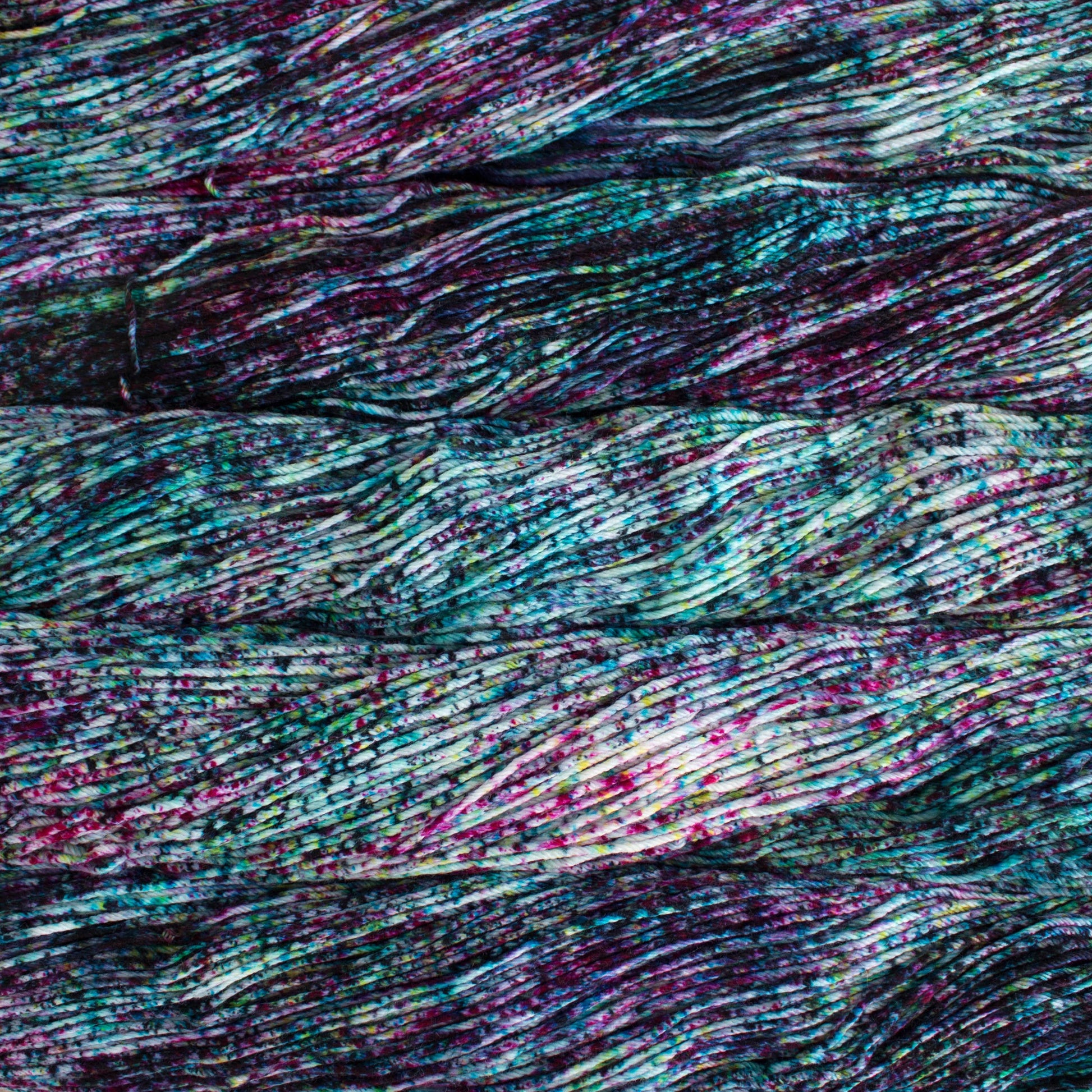 An image of skeins of Malabrigo Arroyo sport weight yarn in an off-white base with speckles of teal and magenta.