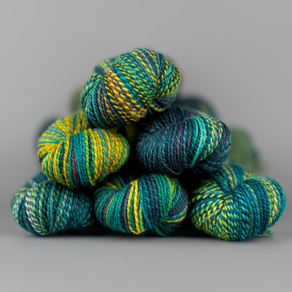 Skeins of Spincycle Dyed in the Wool sport weight yarn in a yellow, green, teal blue, and purple color gradient against a gray background.